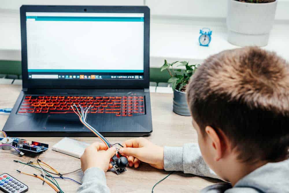 A boy working on an Arduino project with the Arduino IDE open on his laptop