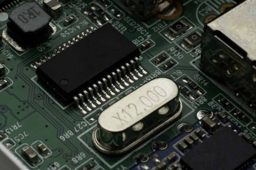 A crystal oscillator mounted close to a microchip on a PCB provides clock signals